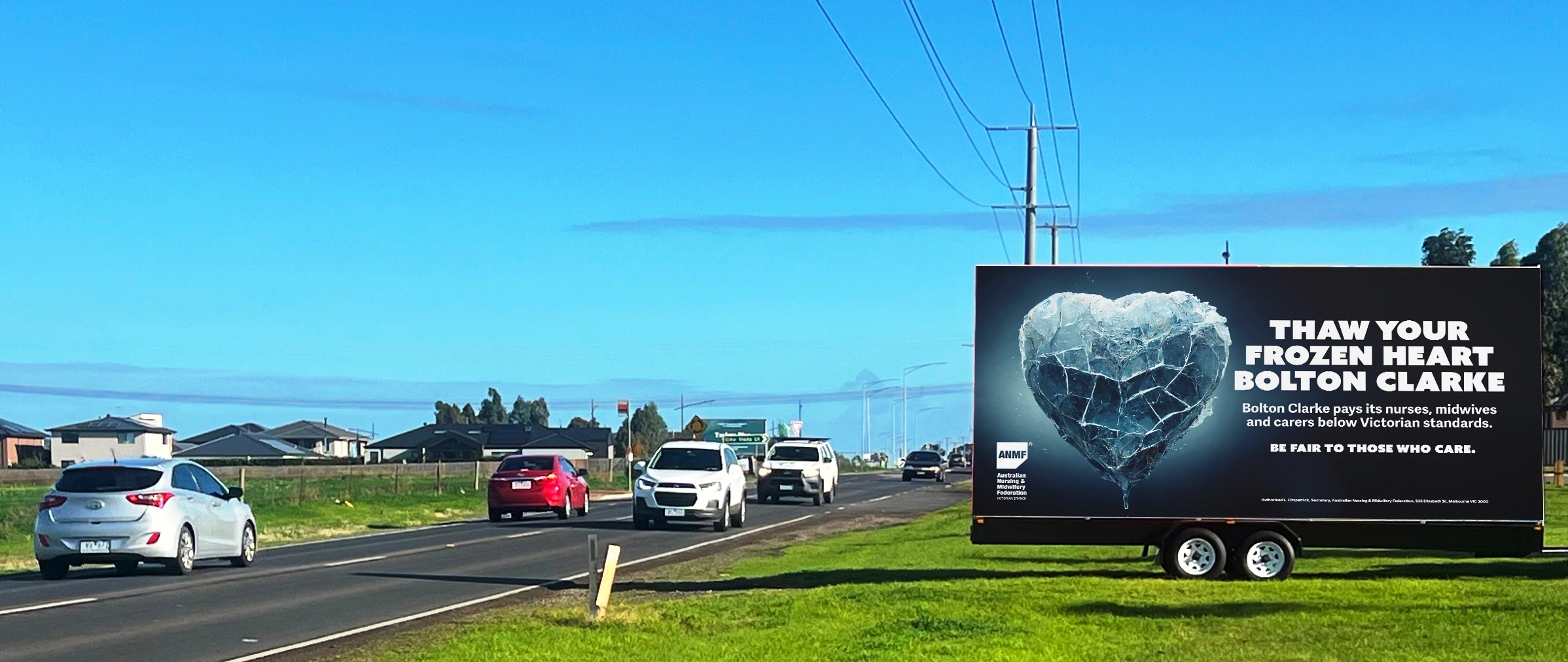 A large mobile trailer billboard displaying a vibrant local advertising campaign parked securely near a busy commercial shopping strip in Australia